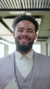 Canlı bir çalışma alanında, kendinden emin bir Afrikalı Amerikalı işadamı karizma ve profesyonellik yayar, dinamik bir çalışma ortamındaki yaklaşımını vurgulamak için içten bir gülümseme sergiler.