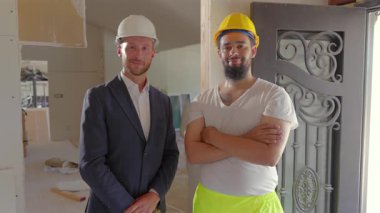 Gelişmekte olan bir iç mekanda, iki farklı inşaat işçisi biri resmi giyinmiş diğeri de iş kıyafeti giymiş olarak yan yana durarak, sektördeki işbirliği çabalarını vurguluyor.