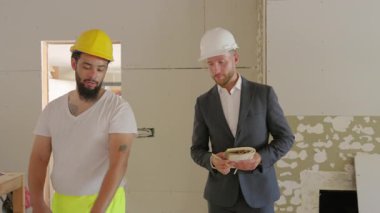 İki farklı inşaat işçisi yoğun bir şantiyede anlamlı bir sohbete dalmış, farklı stilleri ve görevlerine yaklaşımları arasındaki hayati işbirliğini sergiliyorlar.