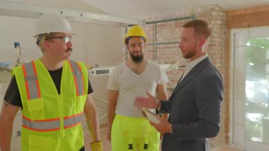 Çeşitli inşaat işçileri proje tartışmasında bir işadamıyla işbirliği yapıyor, yoğun bir şantiyede ortaklıklarını el sıkışarak mühürlüyor, sanayideki başarılarını vurguluyorlar.