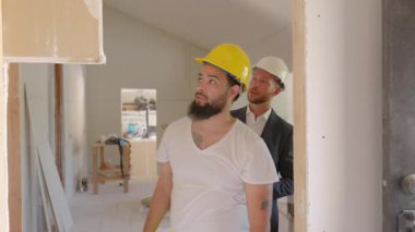 Kısmen yenilenmiş bir alanda, iki inşaat işçisi proje planlarını tartışıyor, çalışmalarının başarılı bir şekilde yürütülmesi ve etkili bir sonuç alınabilmesi için her detayı titizlikle ele alıyorlar.