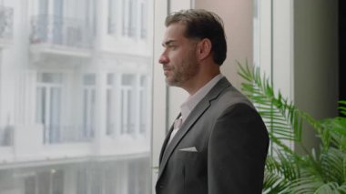 Çağdaş ofis dekorasyonu, iş adamı büyük bir pencerenin kenarında durup, telefonuyla konuşuyor ve dizüstü bilgisayarını tutuyor. Ulaşmak için çabaladığı hırslı hedefler ve isteklerle dolu.