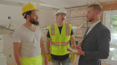 Becerikli inşaat yöneticisi, yoğun bir yenileme şantiyesinde uygun güvenlik donanımı giyen dalgıçlarla gerekli proje özellikleri hakkında ayrıntılı bir tartışmaya girişiyor.