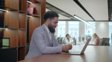 Modern bir iş yerinde, odaklanmış bir Afro-Amerikan işadamı akıllı telefonuyla meşgul olarak, önemli görev ve hedeflere ulaşmaya olan bağlılığını gösteriyor.