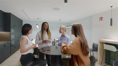 Şık ve modern bir ofis ortamında, çeşitli hırslı iş kadınları kahve molası sırasında arkadaşça ve üretken bir sohbete girişip fikir paylaşıyor ve iş birliği yapıyorlar.