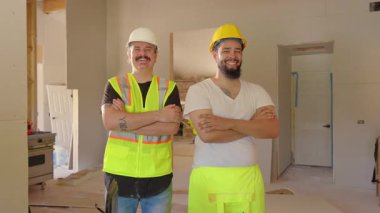 İki neşeli inşaat işçisi, iyi aydınlatılmış bir yenileme alanında birlikte poz vererek, sürmekte olan ilerlemenin ortasında aktif bir inşaat alanında takım çalışması, adanmışlık ve profesyonelliklerini sergilediler.