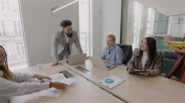 Parlak bir ofiste, çeşitli profesyoneller iş amaçlarına ulaşmak, takım çalışmasının, liderliğin ve iletişimin değerini gözler önüne sermek, bilgisayarlarında beyin fırtınası yapmak ve fikirlerini paylaşmak için işbirliği yapıyorlar.