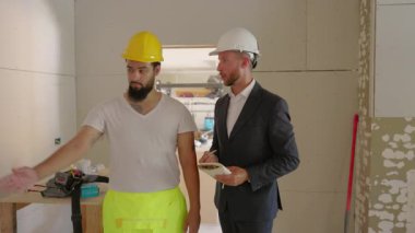 İki inşaat işçisi, uzmanlıklarını vurgulayan bir yenileme ortamında önemli proje detayları, takım çalışması ve yönetim becerilerinin sergilenmesi hakkında derin bir tartışmaya giriştiler