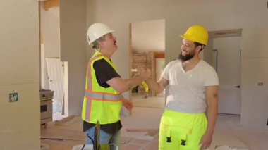 İki neşeli inşaat işçisi enerjik bir şekilde bir beşliği paylaşıyor, coşkulu bir inşaat sahasında sevinçle takım çalışmalarını kutluyorlar. Pozitif, heyecan ve başarı duygusu ile dolu.