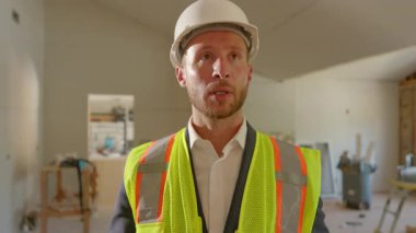 Çelik yelek giyen bir inşaat yöneticisi, önemli proje detaylarını ekibe açıklarken, modern inşaatlarda net iletişim ve profesyonelliğe duyulan ihtiyacı vurguladı