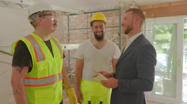 Proje yöneticisi çeşitli inşaat işçileriyle bir yenileme üzerinde çalışarak, iş boyunca verimli ilerleme sağlamak ve güvenliği sağlamak için kilit proje detayları ve güvenlik protokollerini tartışıyor