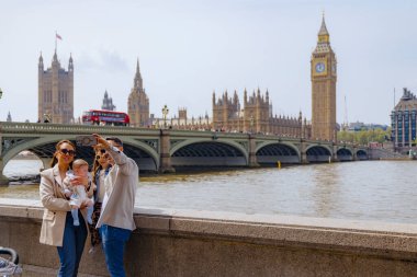 Londra 30.04.2025. Neşe dolu aile Thames nehrinin kenarında harika bir gün geçiriyor. Burada ikonik Big Ben ve Westminster 'ın görkemli sarayı ile harika bir anı yakalıyorlar.