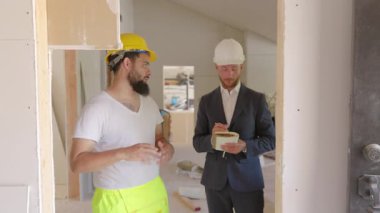 Bir inşaat işçisi ve bir mimar, kısmen tamamlanmış bir yapının planlarını tartışarak, başarılı inşaat sonuçlarına ulaşmada işbirliği ve takım çalışmasının önemini vurguladılar.