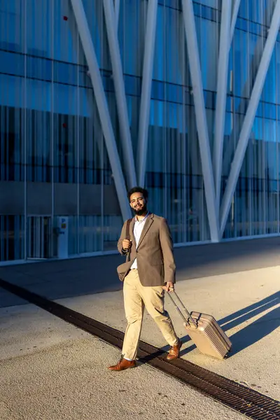 Zarif bir bavulu olan iyi giyimli bir işadamı, çarpıcı bir çağdaş binanın önünde rahatça geziniyor. Canlı, hareketli bir şehir ortamında profesyonellik ve kendine güven gösteriyor.