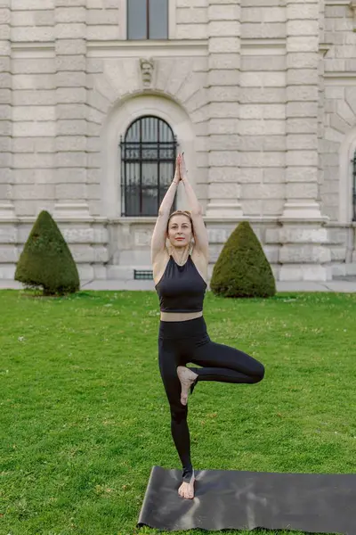 Açık havada yoga yapan bir kadın çarpıcı bir doğal mekanda denge ve sükunetini çok güzel bir şekilde sergiliyor. Bu esnada da manzarayı daha da güzelleştiren tarihi bir binanın yanında.