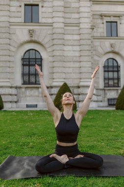 Göçmen bir kız dışarıda yoga yapıyor, doğaya tamamen dalmış ve çarpıcı bir mimariyle çerçevelenmiş, sükunet, zindelik ve farkındalık hissini mükemmel bir şekilde yakalıyor.