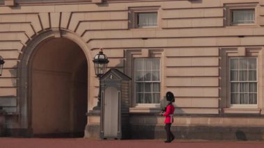 Londra 04.28.2025. Kraliyet muhafızı, çarpıcı kırmızı üniformalı, zarif bir şekilde Buckingham Sarayı 'nın büyük girişinden geçiyor, gerçekten büyüleyici bir sahne, gün ışığıyla mükemmel aydınlatılıyor.