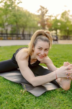 Sakin bir ortamda, orta yaşlı bir kadın dışarıda yoga yapıyor. Esnekliğini ve sağlıklı bir yaşam tarzına olan bağlılığını, çevresini çevreleyen doğanın güzelliğinin ortasında gösteriyor.