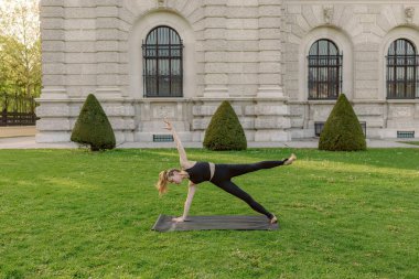Güzel bir açık hava ortamında, orta yaşlı bir kadın yoga yapar, doğayı kucaklarken gücünü ve dengesini gösterir, atmosferin sükunetini ve huzurunu artırır.