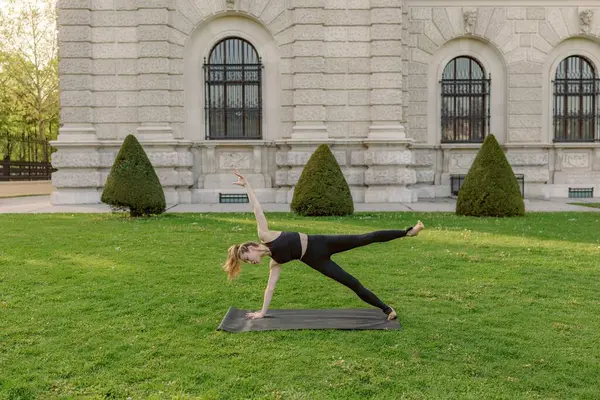 Güzel bir açık hava ortamında, orta yaşlı bir kadın yoga yapar, doğayı kucaklarken gücünü ve dengesini gösterir, atmosferin sükunetini ve huzurunu artırır.