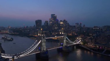 Hava görüntülerinde Tower Köprüsü ve alacakaranlıkta canlı Londra silueti yer alıyor. Thames Nehri 'nin bu ikonik yapıların altında akan ve şehrin güzelliğini tanımlayan sakin bir şekilde parıldıyor.