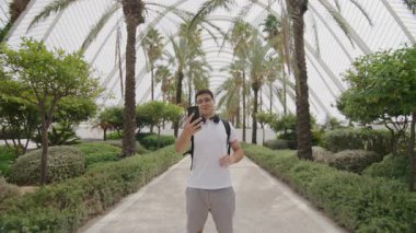 Kulaklıkları ve sırt çantasıyla dışarıda selfie çeken aktif bir genç. Moda, genç blog yazarı egzotik doğal ortamda seyahat ederken videolar yayınlıyor. Yüksek kalite 4k görüntü