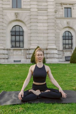 Midadlı bir kadın dışarıda yoga yapıyor, sükuneti ve odaklanmayı somutlaştırıyor. Paspasına odaklanmış halde, kendisini farkındalığa ve etrafındaki barışçıl doğaya daldırıyor, rahatlamasını arttırıyor.