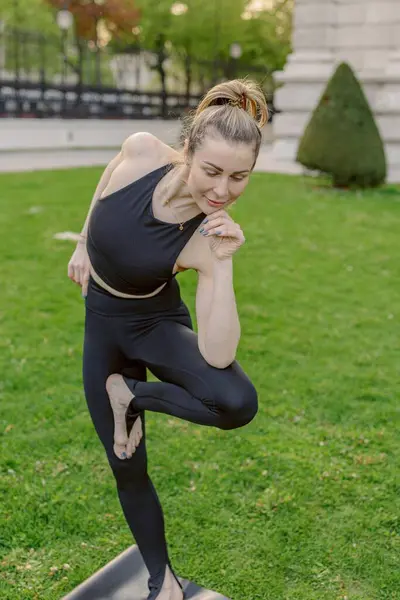 Barışçıl bir açık hava ortamında, genç bir kadın yoga pratiğiyle meşgul, zarafetini ustalıkla sergiliyor ve çevresini saran yemyeşil güzelliğin sakin güzelliğinin arasında sarsılmaz bir şekilde odaklanıyor.