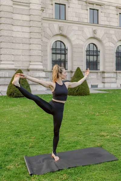 Midadlı bir kadın açık hava yoga seansına katılır, güzel bir doğal ortamda esneklik ve denge gösterir, fiziksel ve zihinsel refahını arttırır, huzur ve sükuneti destekler.