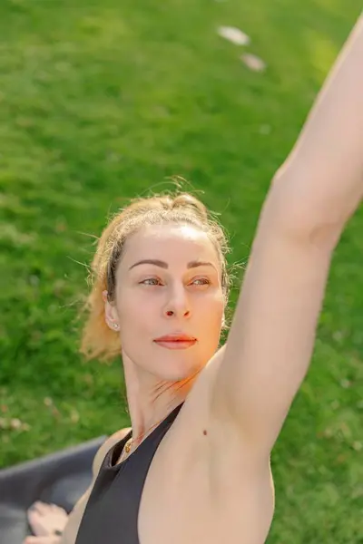 Dışarıda yoga yapan orta yaşlı bir kadın, tamamen sakin ve sakin bir ortama dalmış, genel refahını ve sağlığını iyileştirmek için hareketlerine derinden konsantre oluyor.