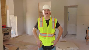 Başlık ve güvenlik yeleği giyen yetenekli bir inşaat işçisi, inşaat ve güvenlik medyası için ideal, profesyonellik ve güvenlik göstergesi olarak, bitmiş bir iç mekanda güven içinde duruyor