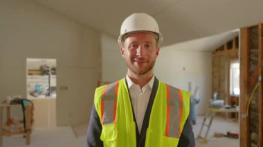 Kaliteli bir inşaat yöneticisi, güvenlik donanımlı, tadilat görmüş bir evde duruyor, güvenli bir çalışma ortamının tüm proje ekibinin güvenliği ve refahı için önemini vurguluyor.