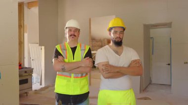 Parlak güvenlik donanımlı iki inşaat işçisi yoğun bir yenileme sahasında güven içinde poz verirken, projede yer alan herkes için güvenlik ve görünürlük sağlarken profesyonellik gösteriyorlar