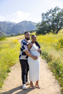 Afro-amerikan açık hava manzarası. Çiftler hamileliklerini sevinçle kutluyor. Sevgi dolu bu özel anda sevgi ve bağlantının özünü yakalıyorlar. 