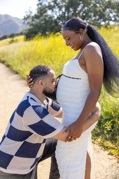 Açık havada afro-amerikan bir çiftin, bu yolculuktaki ebeveynlik sevgisi ve beklentilerini sembolize eden, huzurlu bir ortamda doğacak olan bebeklerini neşeyle kucaklamalarını gösteren fotografı.