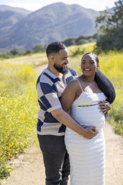 Huzurlu bir ortamda, sevgi dolu bir çift ebeveynlik yolculuklarını kutluyor. Koca, karılarına sarılıyor. İkisi de güzel yaz manzarasında mutluluk saçıyor.