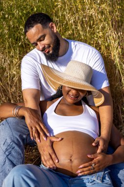 Neşeli ve sevecen bir Afrikalı Amerikalı çift doğanın enfes güzelliğini kucaklarken bu huzurlu anda saf sevgi, sıcaklık ve mutluluk saçan bebeklerini heyecanla bekliyorlar.