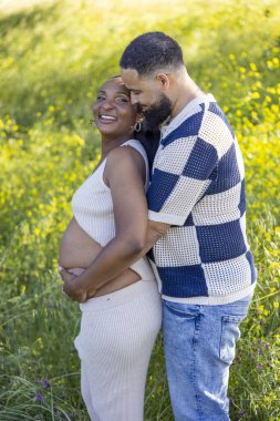 Sevgi dolu ve hamile bir çift, güzel bir yaz gününün keyfini çıkarırken, koca, karısına nazikçe kucak açıyor.