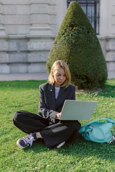 Sakin bir açık hava ortamında, genç bir kadın çimlerin üzerinde oturur, laptopuna odaklanır, işi rahatlıkla dengeler, doğal güzelliğin tadını çıkarırken, hafif esinti ve canlı yeşillikten ilham alır.