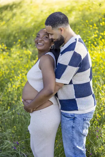 Sevgi dolu ve hamile bir çift, güzel bir yaz gününün keyfini çıkarırken, koca, karısına nazikçe kucak açıyor.