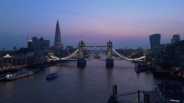 Nefes kesici bir hava aracı, ikonik Tower Köprüsü 'nü, alacakaranlıkta canlı ve çarpıcı Londra silueti ile birlikte, Thames nehrinin akışına karşı mükemmel aydınlatılmış bir şekilde sergiliyor.