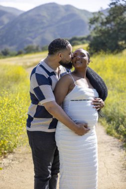 Bu güneşli günde, sevecen bir Afro-Amerikan çifti hamileliklerini sevinçle kutlarken, mutluluğu ve bu özel anda derin bir duygusal bağı paylaşıyor.