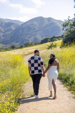 Sevgi dolu bir çift, güzel bir yaz manzarasında mutlu bir şekilde el ele yürüyor, tamamen kucaklıyor ve serin bir açık hava ortamında ebeveynliğe olan güzel yolculuklarını kutluyor.