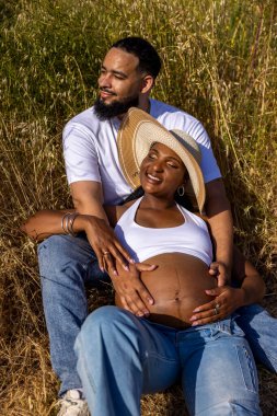 Neşeli bir Afrikalı Amerikalı çift dışarıda güzel bir yaz gününün tadını çıkarıyor. Kocasının şefkatle sarılıp karnını kucaklaması, sevgi ve özen göstermesi...