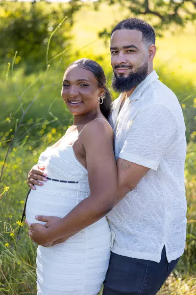 Neşeli ve sevecen hamile bir çift dışarıda güzel bir yaz gününün tadını çıkarıyor. Kocası, eşlerini nazikçe kucaklıyor ve destekliyor. Huzurlu ve barışçıl bir ortamda bebek şişliği büyütüyor.