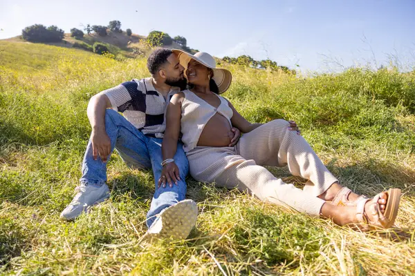 Sevecen bir Afrikalı Amerikalı çift doğadaki hamileliklerini kutluyor. Sıcak güneşin altında, çarpıcı bir yeşillik ve canlı ışığın altında keyifli bir anın tadını çıkarıyorlar.