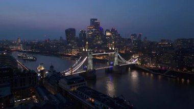 Tower Köprüsü 'nün nefes kesici ve çarpıcı hava manzarasını tecrübe edin. Alacakaranlıkta güzelce aydınlatılıyor. Londra' nın ışıldayan silueti Thames Nehri 'nin ışıldayan suları üzerinde parıldıyor.