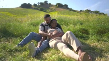 Sevecen bir Afrikalı Amerikalı çift, neşeli bir şekilde güneşli bir günü kucaklıyor, hamileliklerini bereketli, büyüleyici bir ortamda kutluyorlar, mutluluk ve bağlantı yayıyorlar.