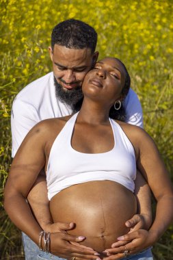 Afrika kökenli Amerikalı bir çift dışarıda hamileliklerini sevinçle kutluyor. Koca, eşlerine kucak açıyor. Yeşillik içinde, büyüyen aileleri için heyecanlı bir ortam yaratıyor.