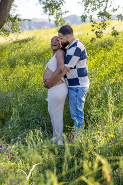 Bu güzel yaz gününde, neşeli bir Afrikalı Amerikalı çift doğanın tadını çıkarıyor. Kocasının hamile eşlerinin karnına sevgiyle sarılıp birlikte geçirdikleri güzel anları kutluyor.